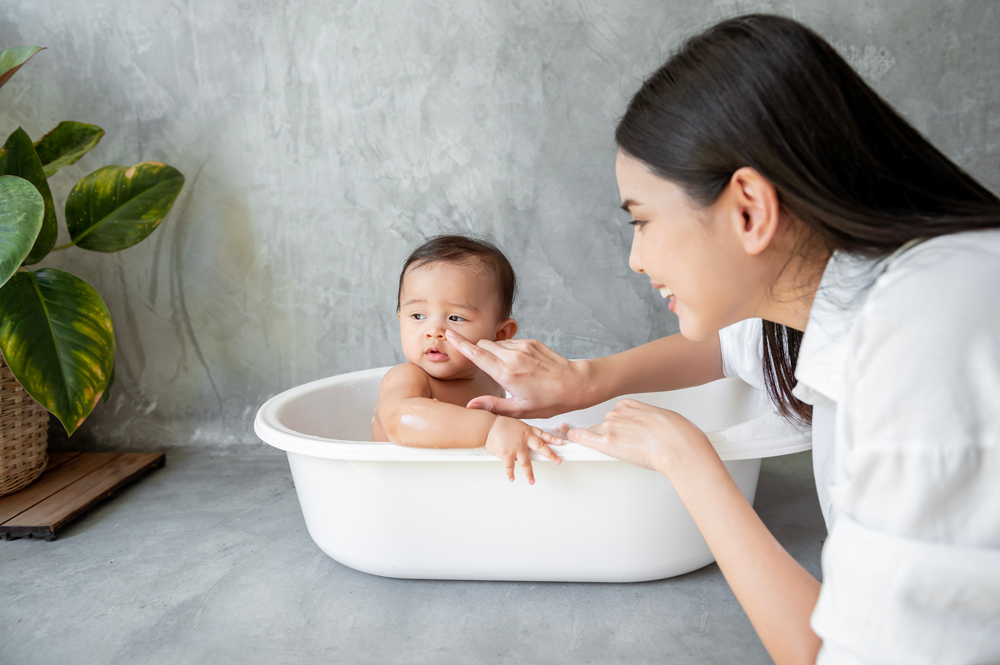 Asian women giving baby bath in little white tub