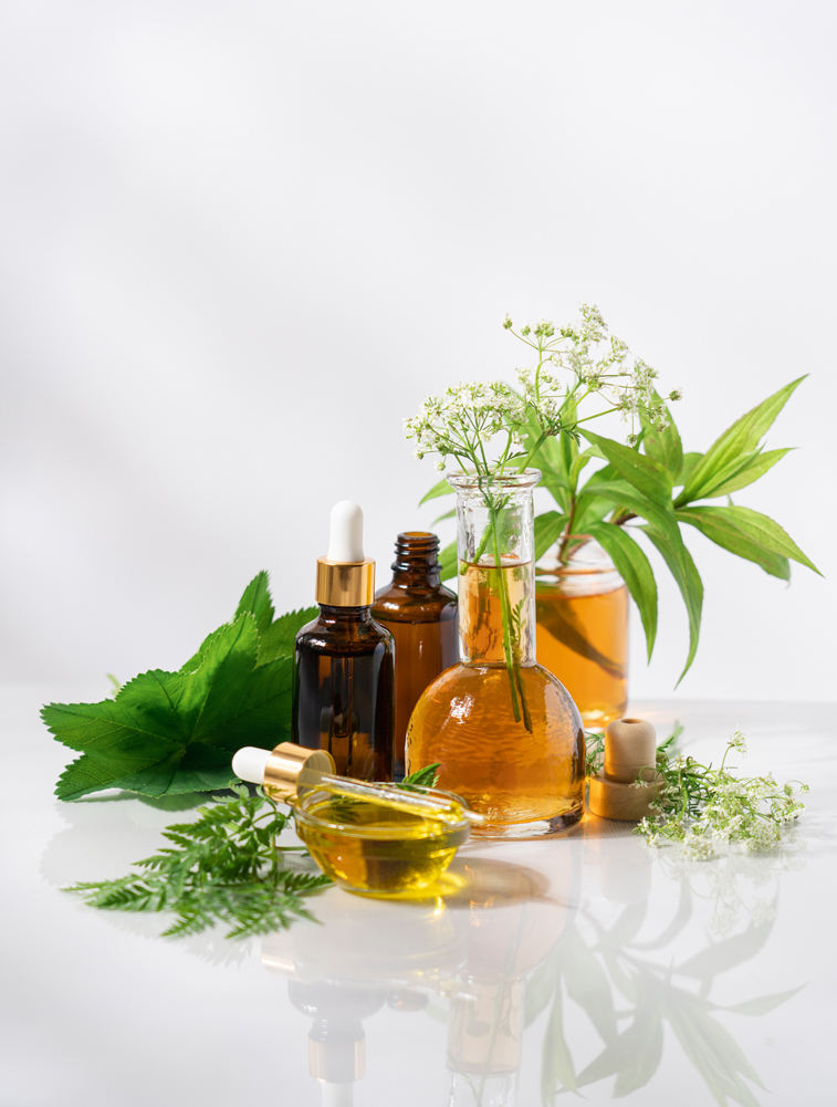 Bottles of essential oils with flowers and greens around them